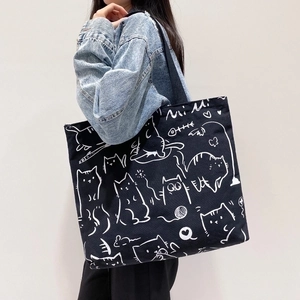 Large black canvas tote bag with white cat illustration worn by a model in casual style