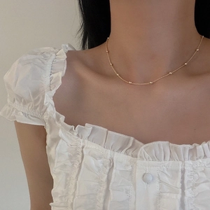 Close-up of a minimalist gold beaded chain necklace worn on the collarbone for daily style