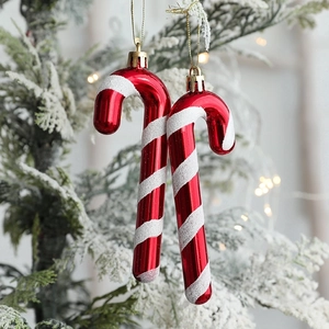 Red and white glittery candy cane Christmas ornaments hanging on a snowy tree branch