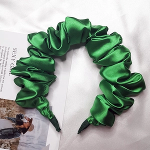 Dettaglio del cerchietto in raso verde smeraldo arricciato con trama in seta su fondo