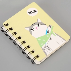 Close-up of yellow A7 notebook with a cartoon cat holding a fish and black spiral binding