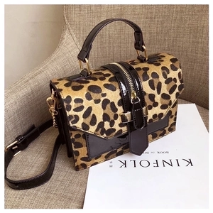 Leopard print crossbody bag with black leather trim and gold hardware on a beige sofa