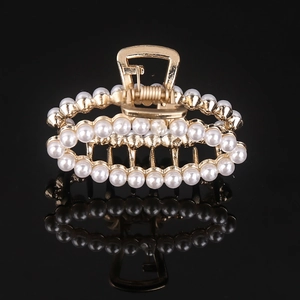 Detail of a golden metal hair claw clip featuring rows of white pearls on a black background