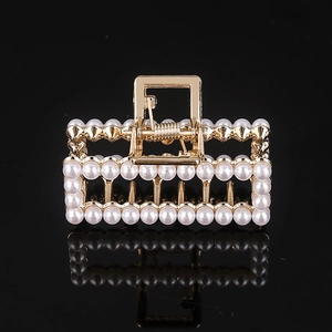 Detail of gold metal hair claw clip with inlaid white pearls on black background