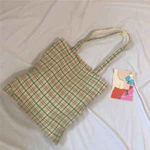 Detail of green and pink plaid canvas tote bag flat lay on white fabric background