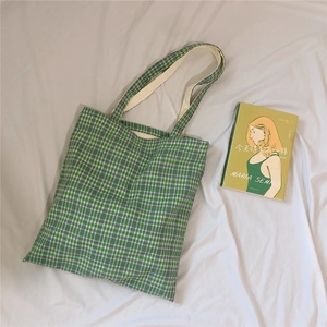 Detail shot of green checkered canvas tote bag laying on white fabric with a book