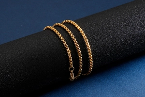 Detail of a golden box chain necklace draped on a textured black jewelry display stand