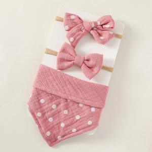 Detailed view of pink polka dot cotton bib and two soft bow headbands for newborns
