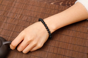 Close-up of matte black agate beaded bracelet worn on wrist with Zen style background