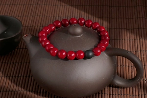 Detail of red natural stone beads bracelet with black matte bead on a dark teapot lid