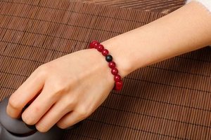 Close-up of red stone beaded bracelet with black agate accent on wrist with bamboo background