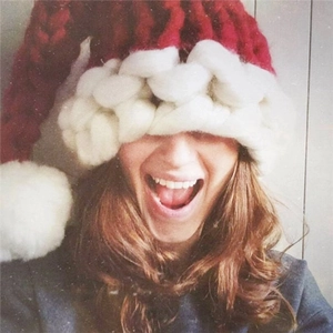 Handmade red chunky knit Christmas hat with white brim worn by a smiling model