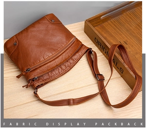 Detail of a brown leather shoulder bag with dual zippers and adjustable strap on a wood table