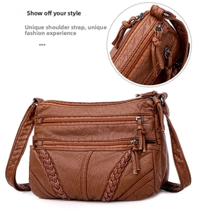 Close-up of brown soft leather crossbody bag showing multi-zipper layers and woven details