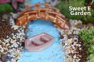 Macro detail of miniature resin boat and arch bridge on blue sand moss micro landscape