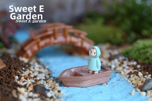 Macro shot of a resin miniature girl in green raincoat standing on a wooden texture boat