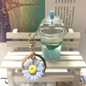 Detail of mini milk tea cup keychain with blue liquid and purple daisy on a white bench