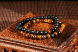 Close-up of tiger eye and matte black agate beaded bracelets on a vintage wooden base