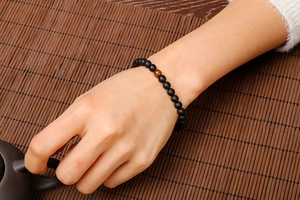 Detailed view of matte black onyx beaded bracelet with a single tiger eye stone on a wrist