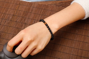 Tiger eye and matte agate beaded bracelet worn on wrist over a bamboo mat background
