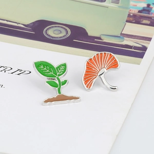 Detail view of green sprout and orange ginkgo leaf enamel pins with silver metal borders