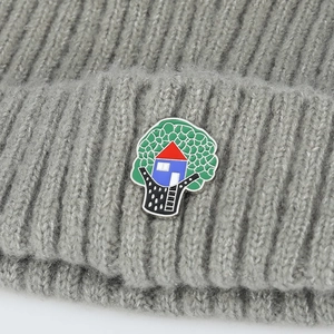 Macro shot of an enamel green tree and red house brooch on a grey knitted beanie hat