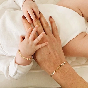 Close-up of matching gold disc chain bracelets worn by an adult and a baby on white background