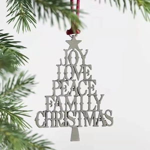 Silver metal Christmas tree ornament with engraved words hanging on a green pine branch