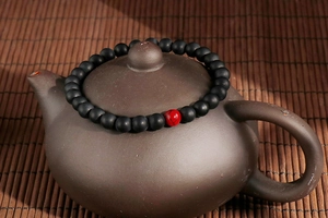 Macro detail of matte black agate beads with red cinnabar accent on a tea lid