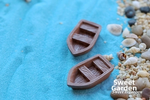 Detail of two miniature resin rowboats with wood texture on a blue sand beach scene