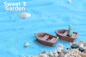 Miniature resin boat figurines with little human figures on blue sand beach scenery