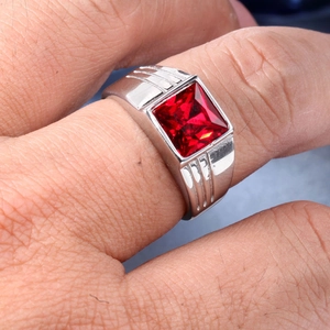 Macro detail of men's silver stainless steel ring with square red gemstone on finger