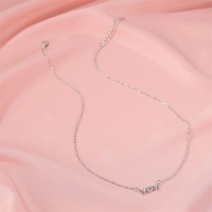 Détail du collier MOM en argent avec incrustation de zircone sur un fond en soie rose