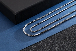 Macro shot of silver box chain necklace on blue textured surface with high gloss finish