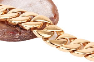 Detailed macro shot of thick polished gold-plated Cuban link chain on agate stone
