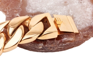 Macro view of a polished gold lobster clasp closure on a heavy stainless steel chain