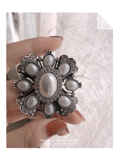 Detailed close-up of a baroque pearl brooch with rhinestones held in hand against curtains