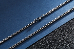 Macro shot of silver stainless steel Cuban chain necklace with lobster clasp on dark texture