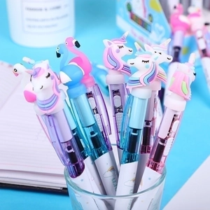 Cute luminous unicorn and flamingo ballpoint pens in a glass holder on a blue desk