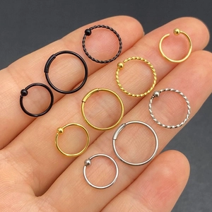 Surgical steel nose rings and hoop earrings in black gold and silver on fingers