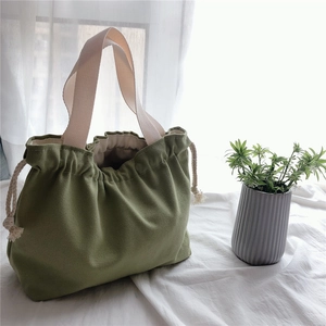 Detail of green canvas drawstring handbag featuring thick woven handles and cotton rope closure