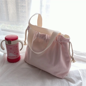 Detail of pink drawstring canvas tote bag with cotton tassels on a bright windowsill