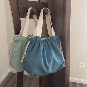Detail of mint green and blue canvas drawstring tote bags hanging on a wooden rack