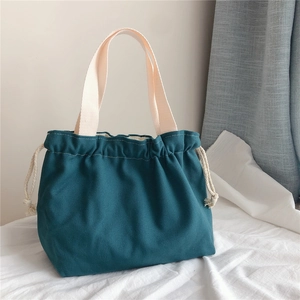Detail of dark green canvas drawstring handbag with sturdy beige woven handles and stitching