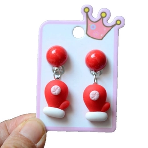 Close-up of festive red Christmas glove earrings held in hand with white crown card