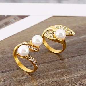 Exaggerated golden leaf rings with white pearls and sparkling crystals on wooden surface