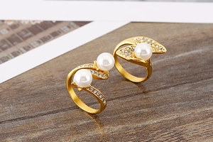 Detail of gold titanium rings with pearls and sparkling rhinestones on wood