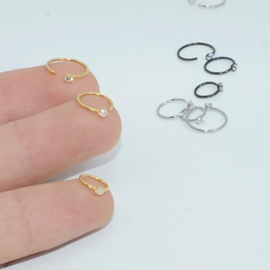 Macro detail of multi-size C-shaped cubic zirconia nose rings in gold, silver, and black metal