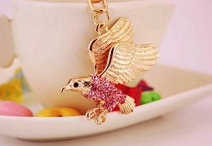 Detailansicht eines goldenen Adler-Schlüsselanhängers mit rosa Strass auf einer Tasse