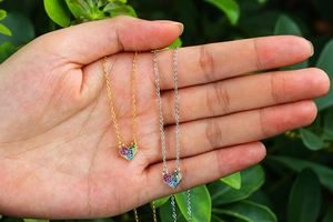 Close-up of gold and silver heart necklaces with colorful crystals against green leaves